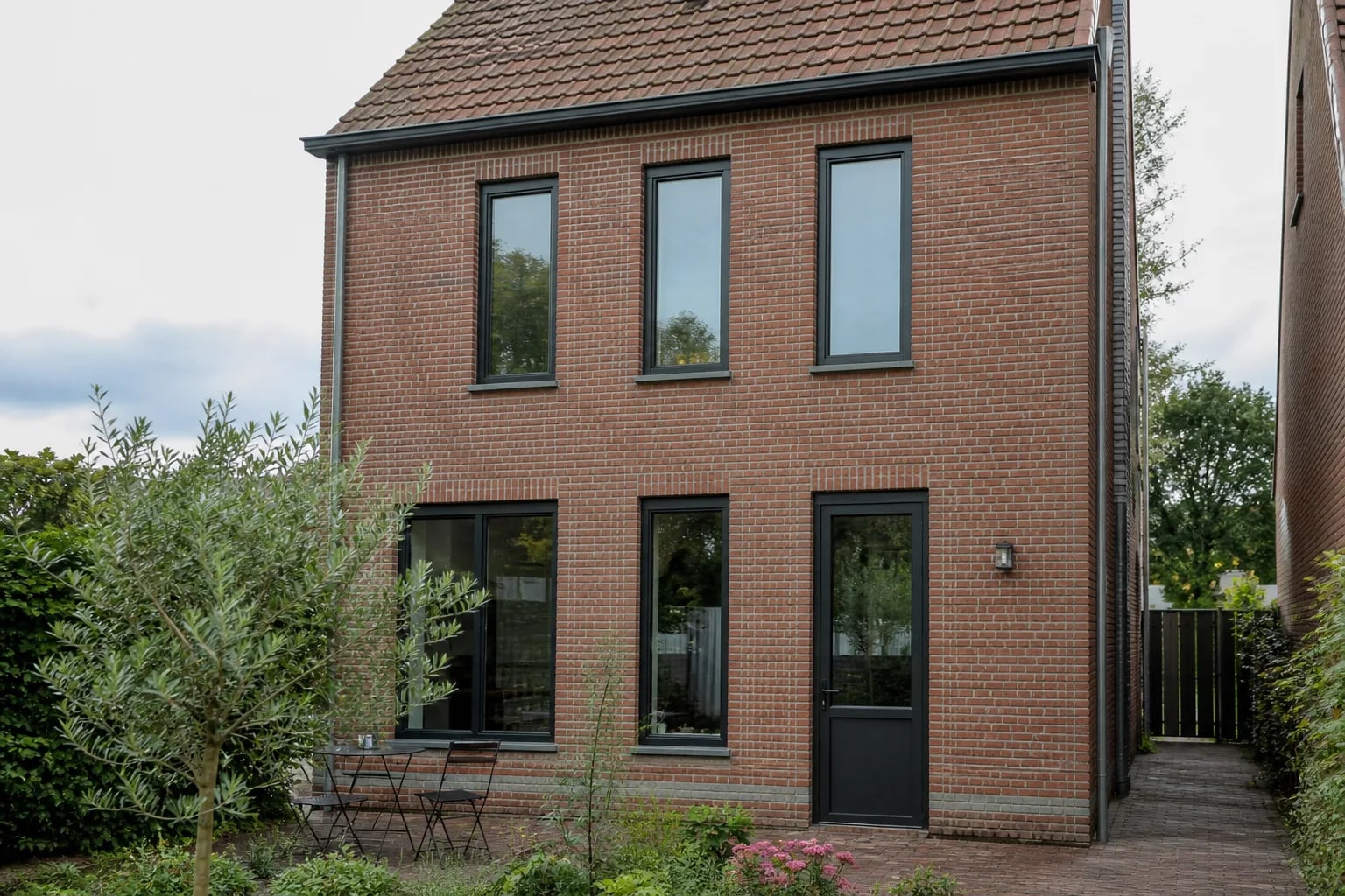 Architectonische bakstenen woning met slanke donkere staal-look kozijnen en een glazen achterdeur